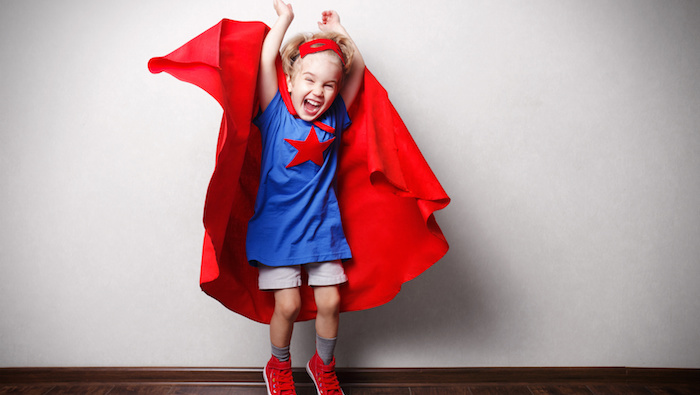 Happy child in superhero suit against gray wall.