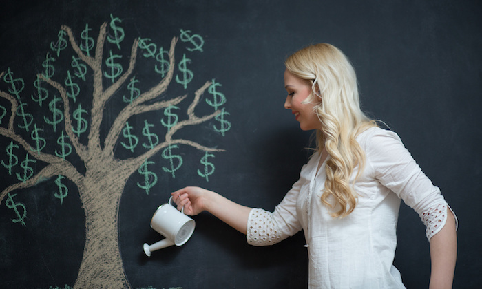 Happy blonde Business woman in front of chalk money tree drawing on blackboard.