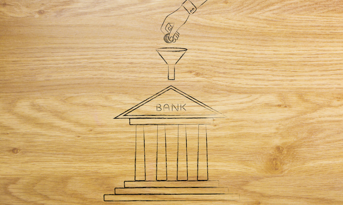 hand dropping coins into funnel above bank building