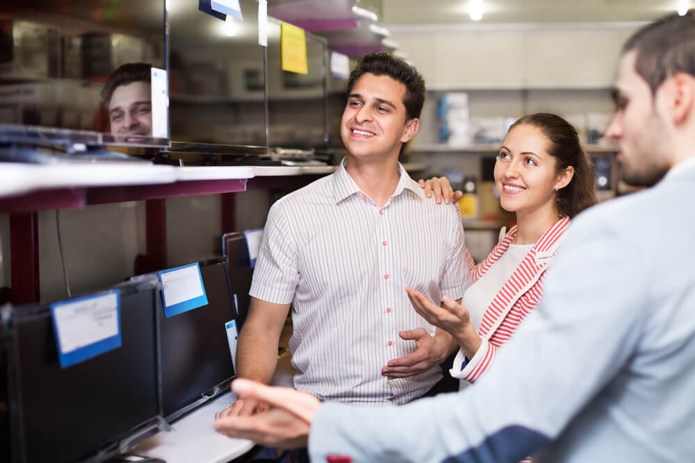 atendente mostrando produtos para casal de clientes
