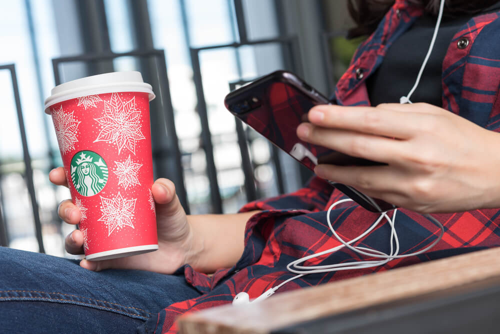 garota segurando copo da empresa starbucks enquanto acessa smartphone