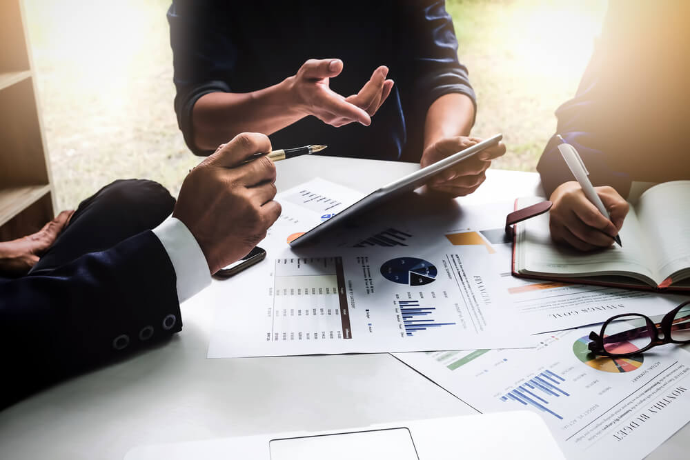 profissionais de marketing sentados em mesa executiva com tablet e papeis com estatisticas 