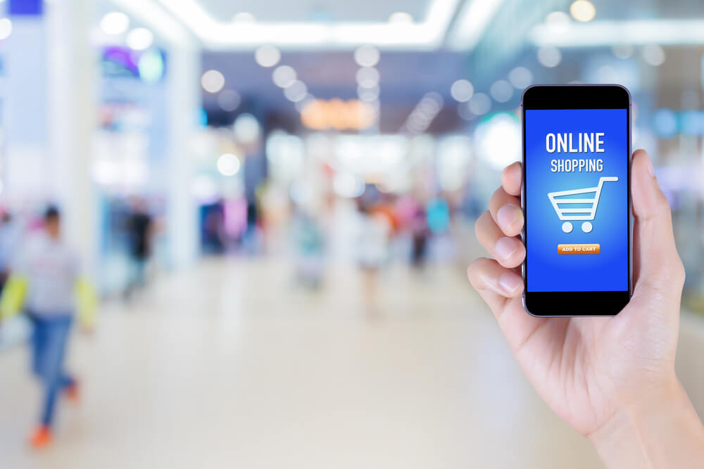 mao masculina segurando smartphone com carrinho de compras e palavra online shopping em tela