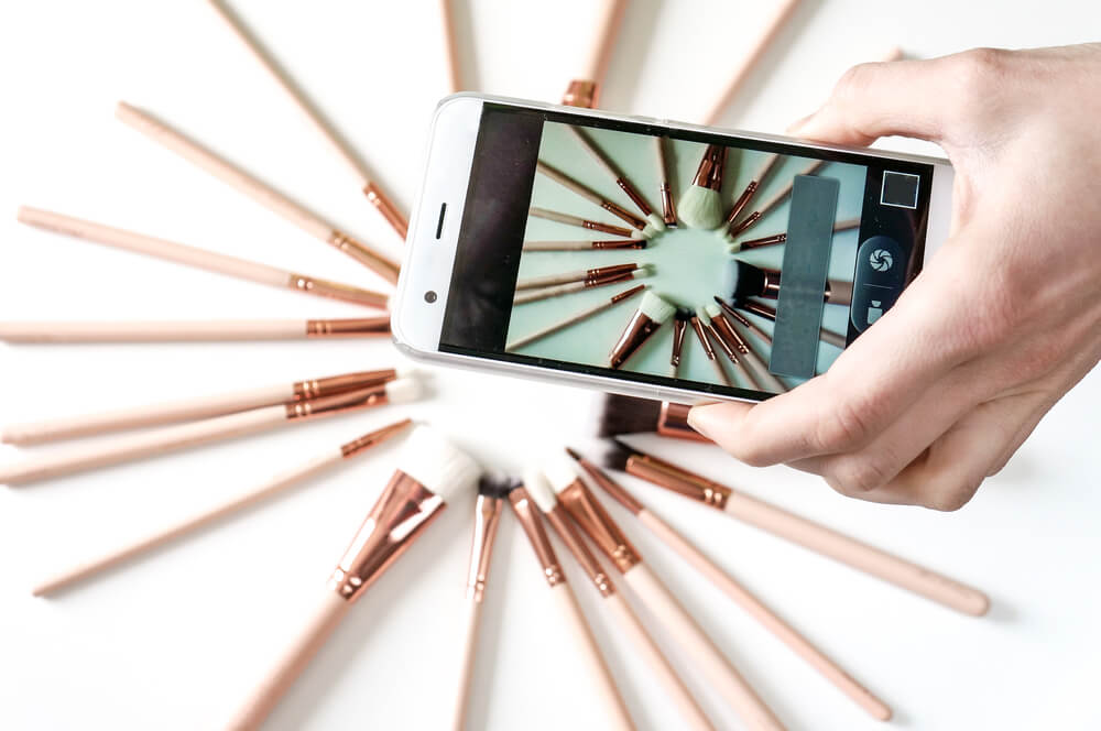 mao segurando smartphone ao tirar foto de produtos sob mesa
