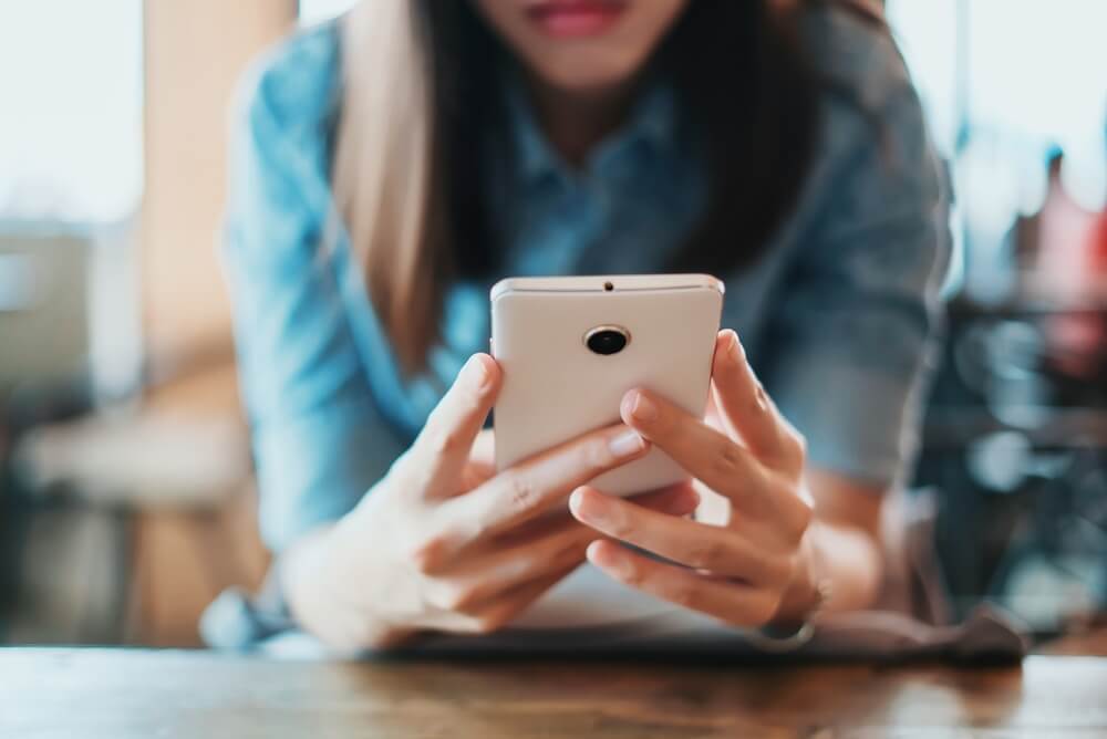 mulher sentada e apoiada em mesa com smartphone em maos