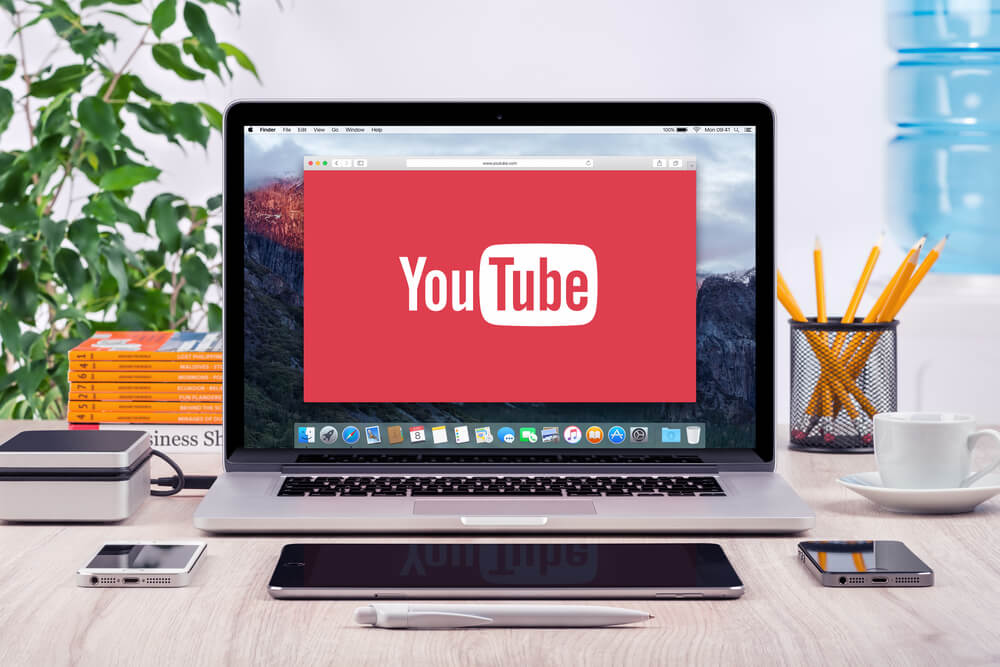 computador em mesa de escritorio com smartphones ao lado e simbolo de aplicativo youtube em tela