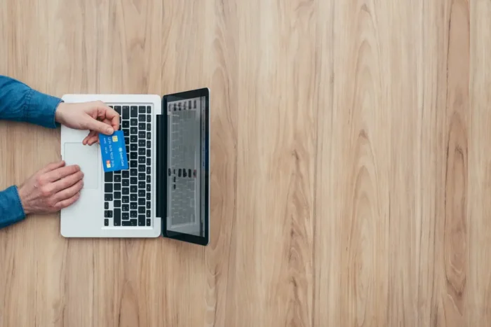 visão de cima de laptop e pessoa segurando cartão de crédito