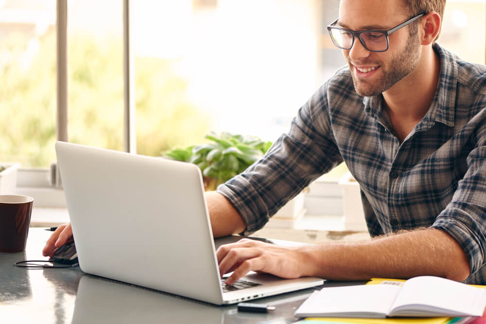 homem em mesa de escritorio teclando em laptop