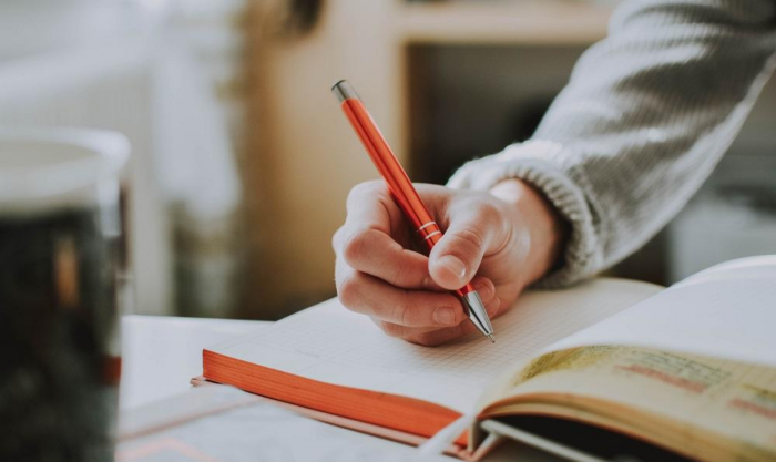 Someone writing in a book with a pen.