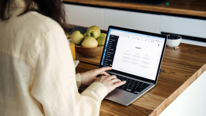 Donna che utilizza ChatGPT su un laptop in casa, scrivendo contenuti digitali a un tavolo di legno